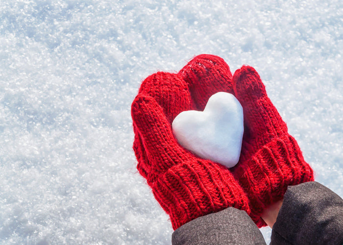 Red mittens holding snow heart.
