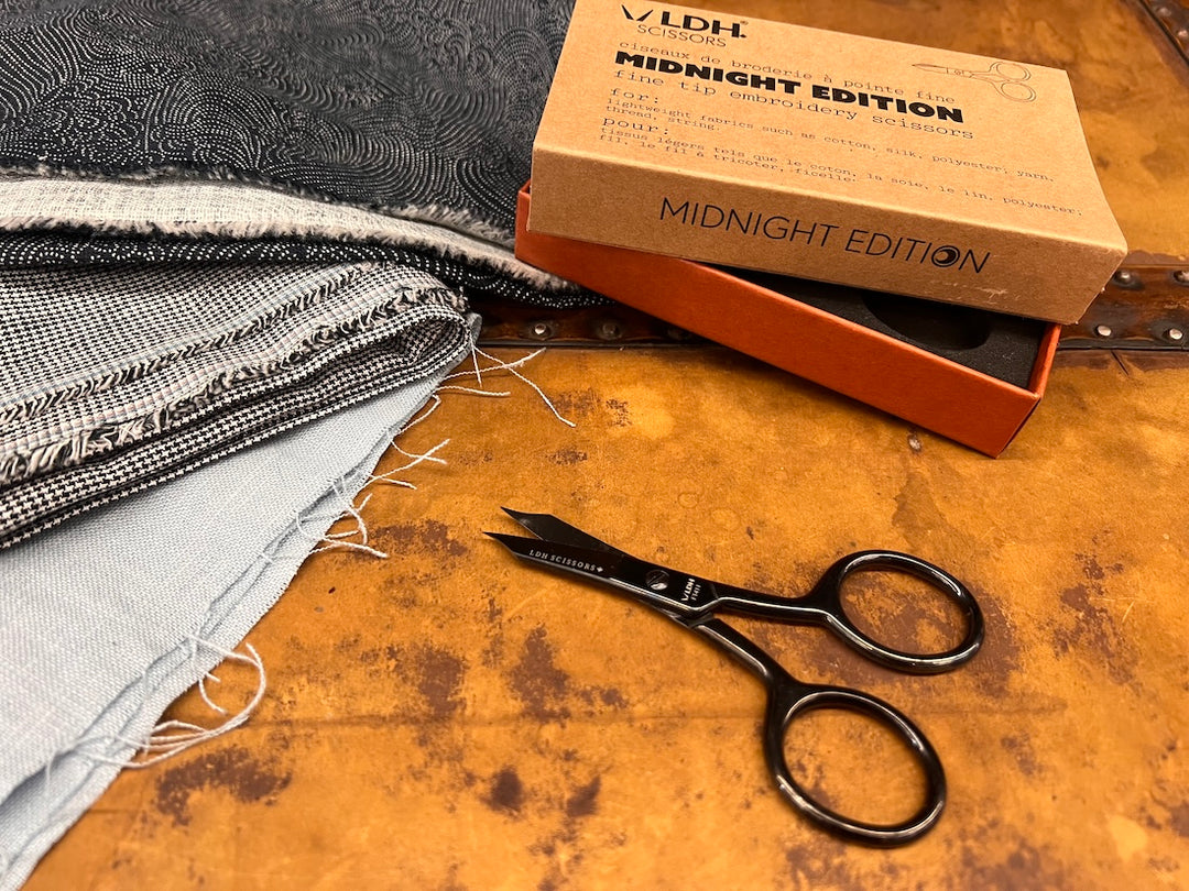 Scissors with their box above them and a stack of fabric to the left.
