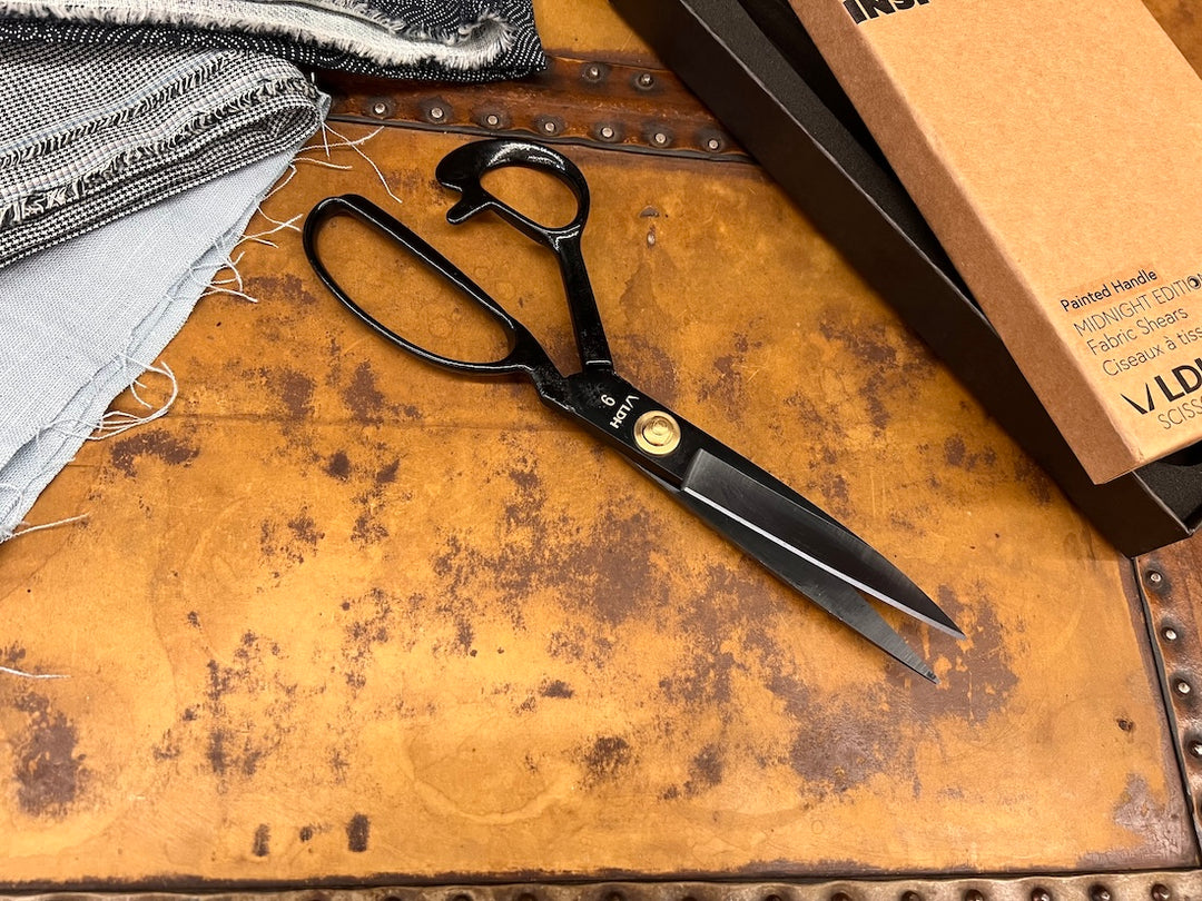 Scissors with their box to the right and a stack of fabric to the left.