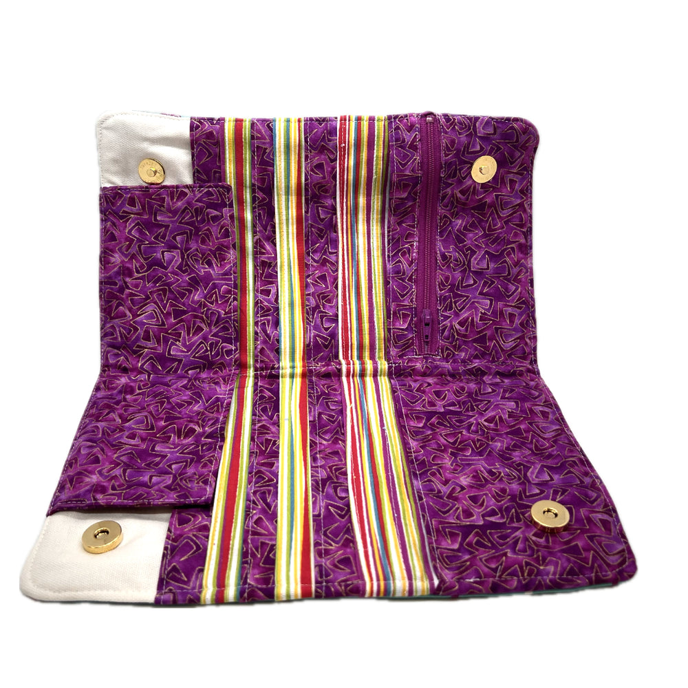 The inside of the needle case the pockets alternate between a purple fabric with geometric patterns and striped fabric with the same purple, green, gold, red, teal, and white. 