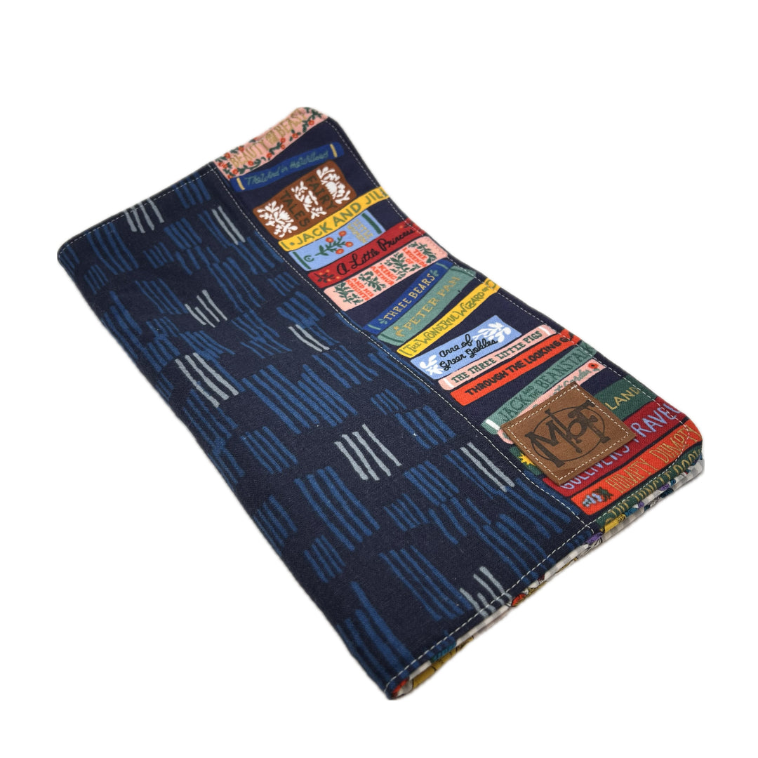 Outside of needle organizer with a dark navy blue base pattern of vertical stripes, decorated with a collage of colorful vintage-style books along one side.