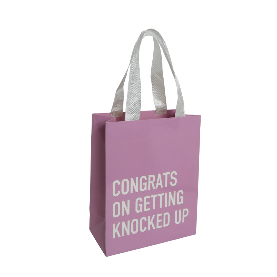 Pink bag with white handles that reads: CONGRATS ON GETTING KNOCKED UP.