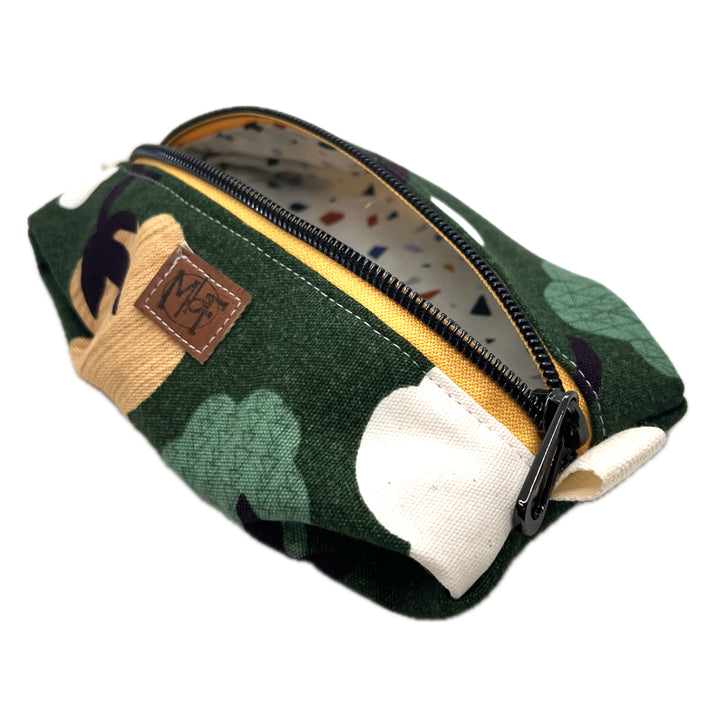 A zippered fabric pouch with cotton plant flowers on a green background. The inside fabric has green, blue, orange, and purple/gray confetti shapes on a cream background. 