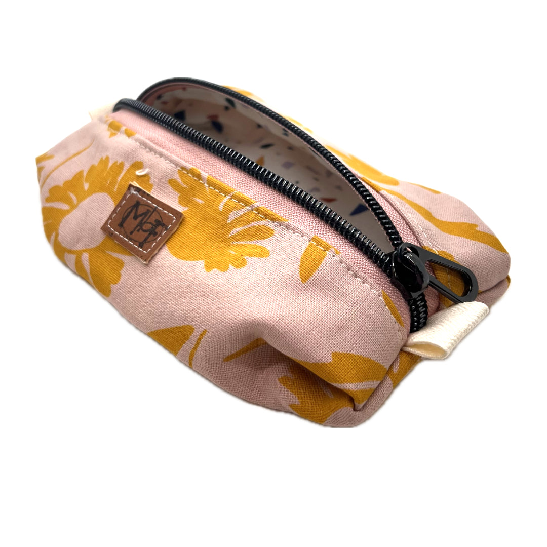 A small zippered pouch with a pink and mustard yellow floral pattern, the fabric on the inside has blue, green, purple/gray, and orange confetti shapes on a white background.