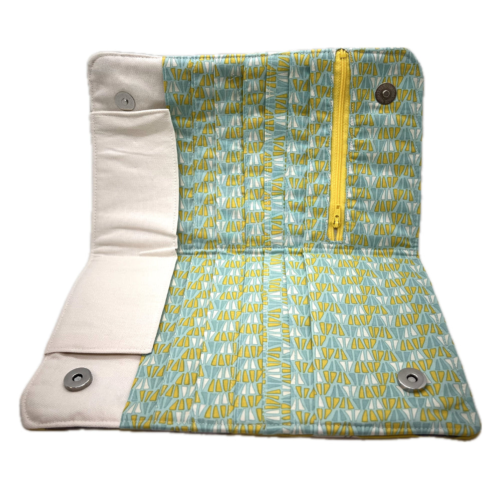 The inside of the needle case in creamy white at the top. The pockets for the needles are in a rows of geometric triangles with blunted top points. The background is a teal, the triangles are in dark teal, creamy white, grinchy green. The zipper on the notions pouch is yellow. 