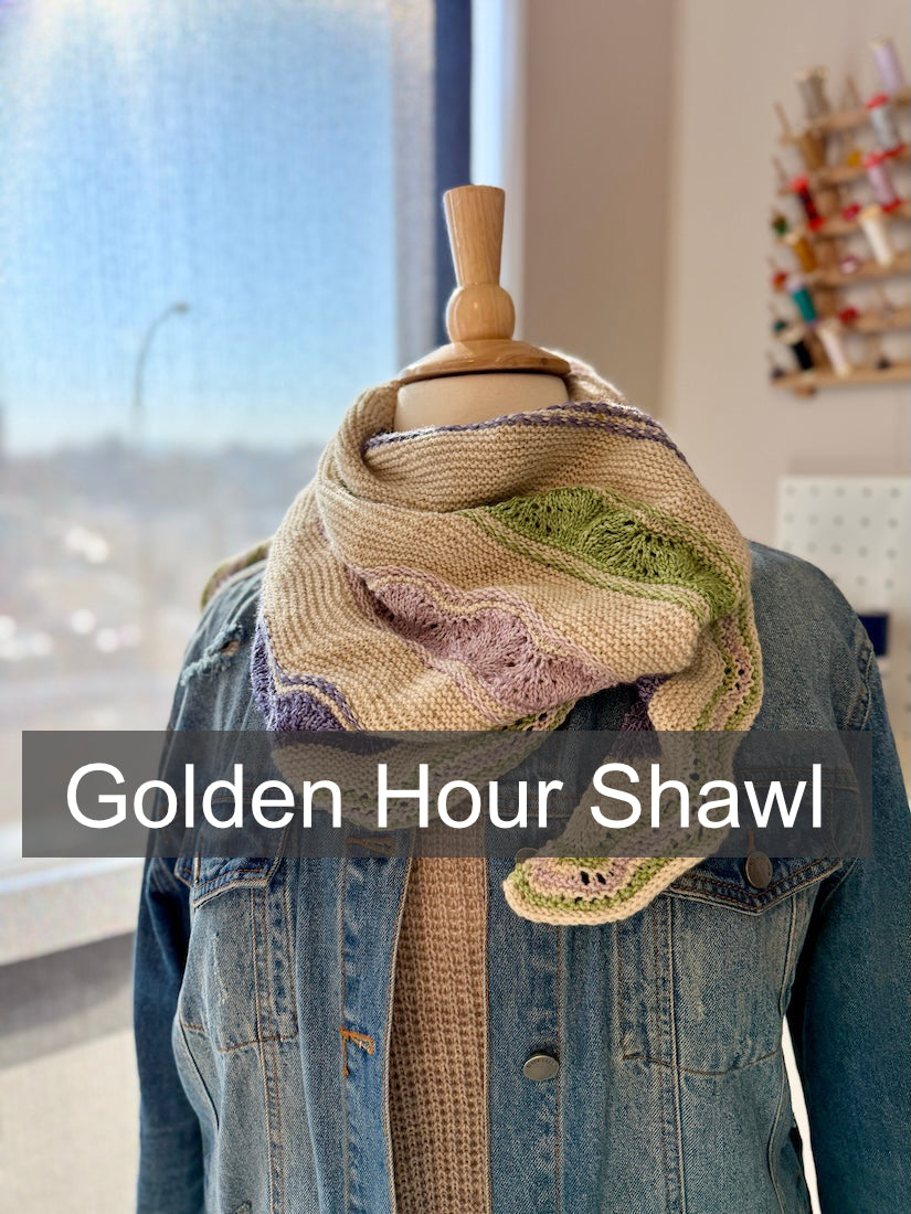 Knitted shawl, named "Golden Hour" draped over a denim jacket with a blurred indoor background.
