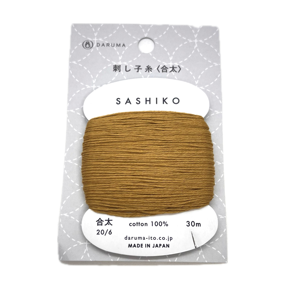 A golden brown cotton thread wrapped around a cardboard bobbin inside a package with clear plastic. 