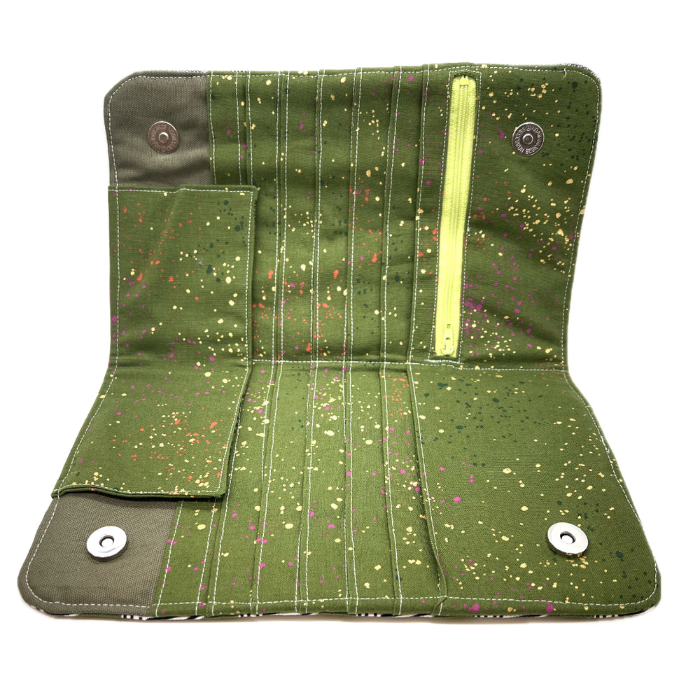 The needle case opened, there's a matching green on the inside with colored drops that look like whimsically spattered paint in gods, hot pinks, and oranges. The zipper is in lime green, and you can see the magnetic snaps. 