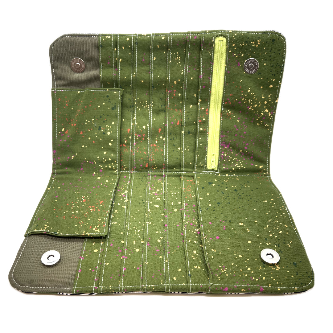 The needle case opened, there's a matching green on the inside with colored drops that look like whimsically spattered paint in gods, hot pinks, and oranges. The zipper is in lime green, and you can see the magnetic snaps. 
