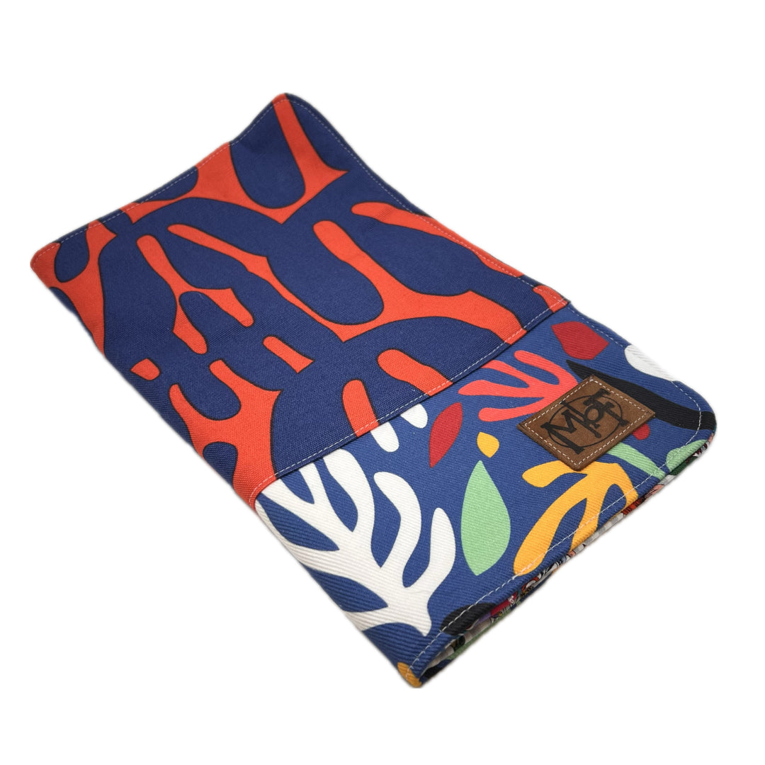 Outside of a needle organizer with a bold abstract pattern in navy blue, coral orange, white, yellow, and green, featuring a brown leather patch with the letters 'MbF' on the lower right edge.