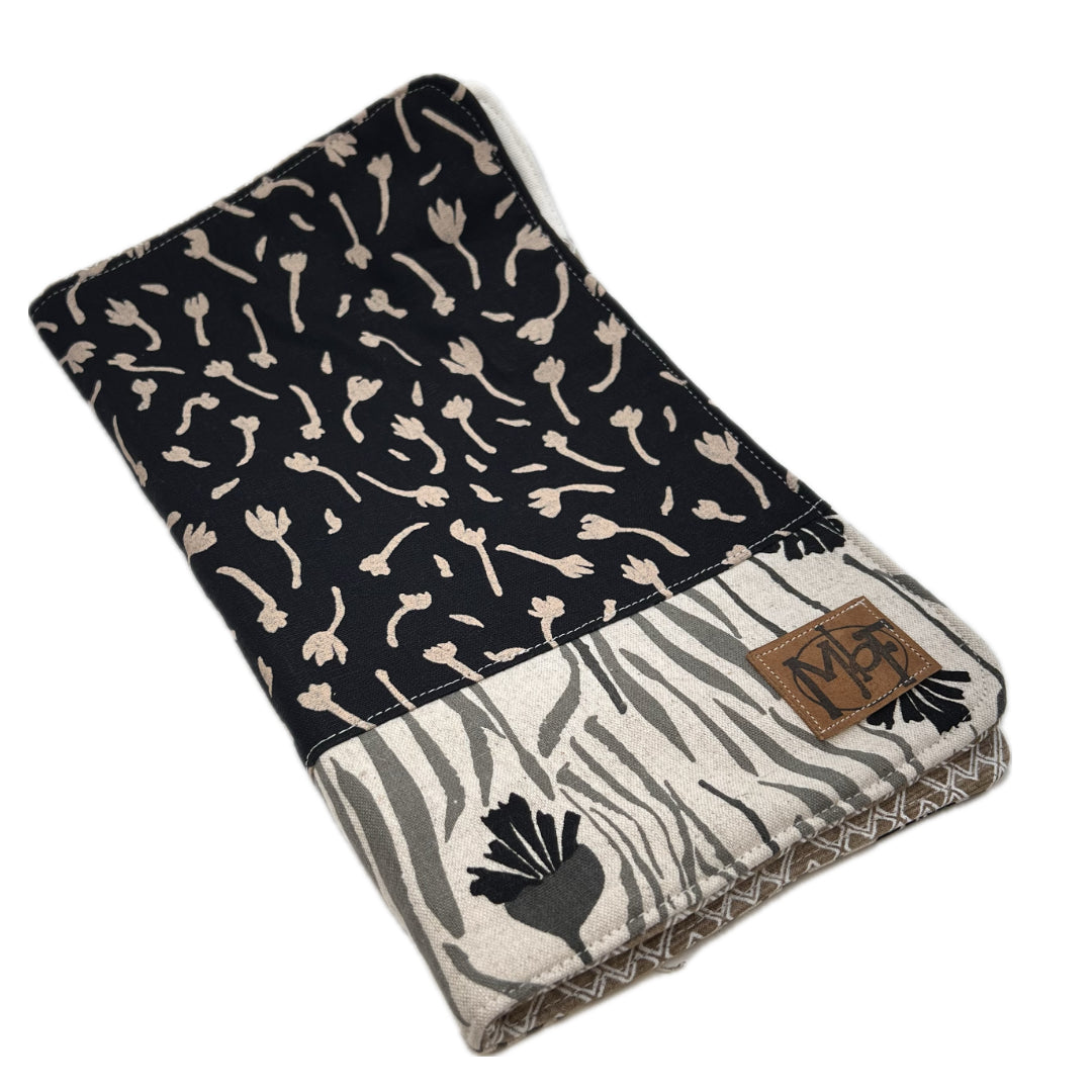 Outside of needle organizer featuring a black top section with beige floral motifs and a lower section with a gray and white zebra print and black floral accents. A brown leather patch with the brand name 'MbF' is sewn onto the side.