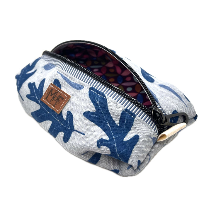 A zippered fabric pouch with a blue oak leaf pattern on a light gray background. The inside fabric has pastel green, teal, pink, orange abstract petal shapes on a purple background. 