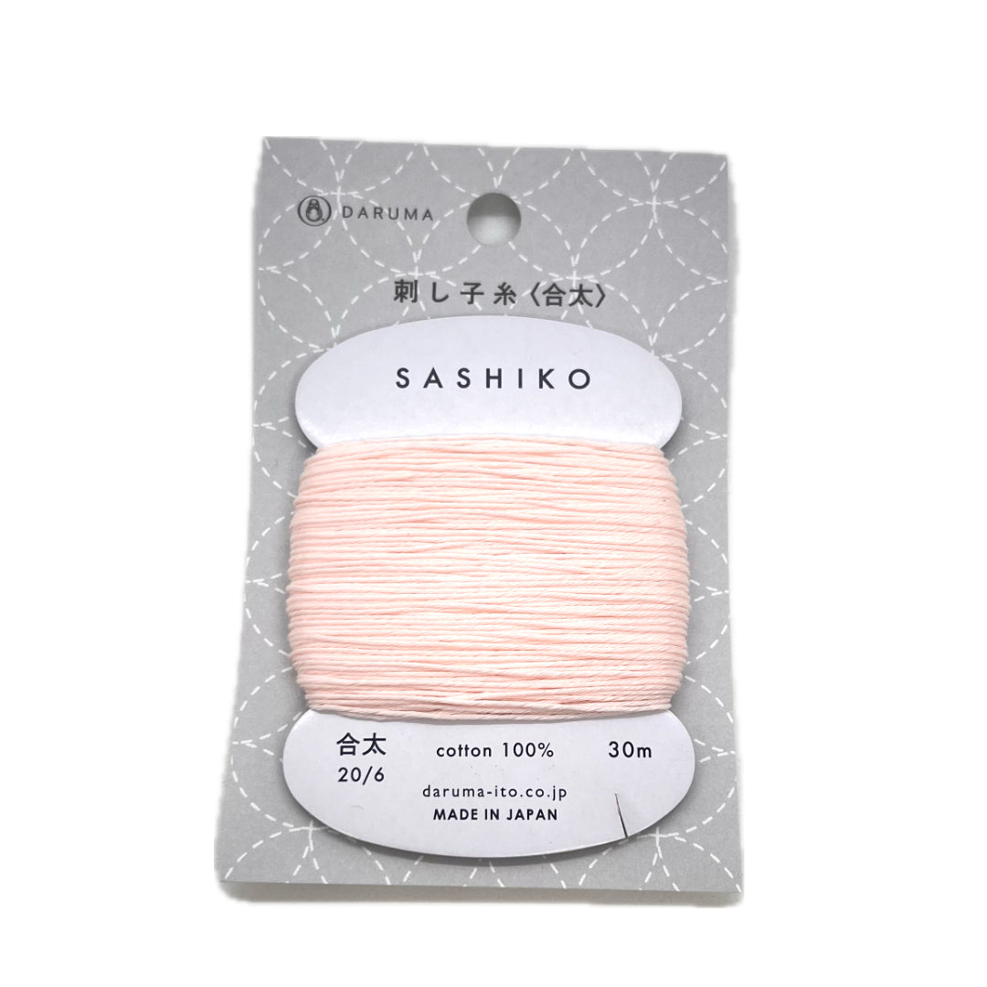 A pale pink cotton thread wrapped around a cardboard bobbin inside a package with clear plastic. 