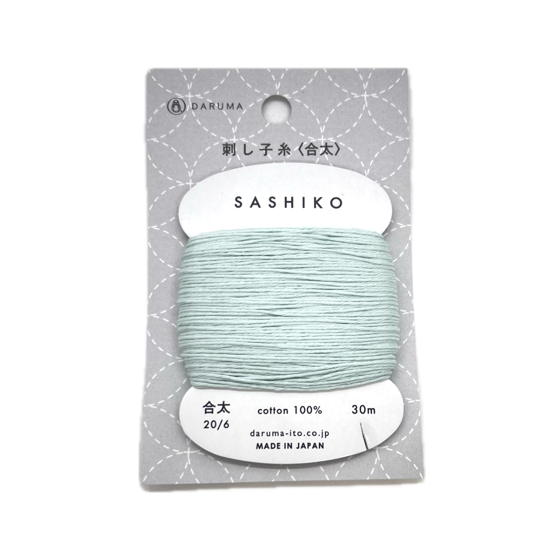 A light teal colored cotton thread wrapped around a cardboard bobbin inside a package with clear plastic. 