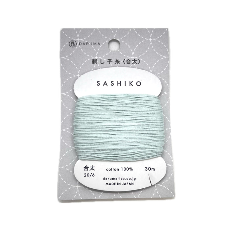 A light teal colored cotton thread wrapped around a cardboard bobbin inside a package with clear plastic. 