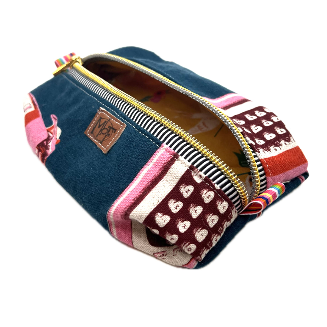 A zippered fabric pouch with pink typewriters on a navy blue background. The inside fabric has white doves carrying banners that say "hope", "love" on a mustard yellow background.