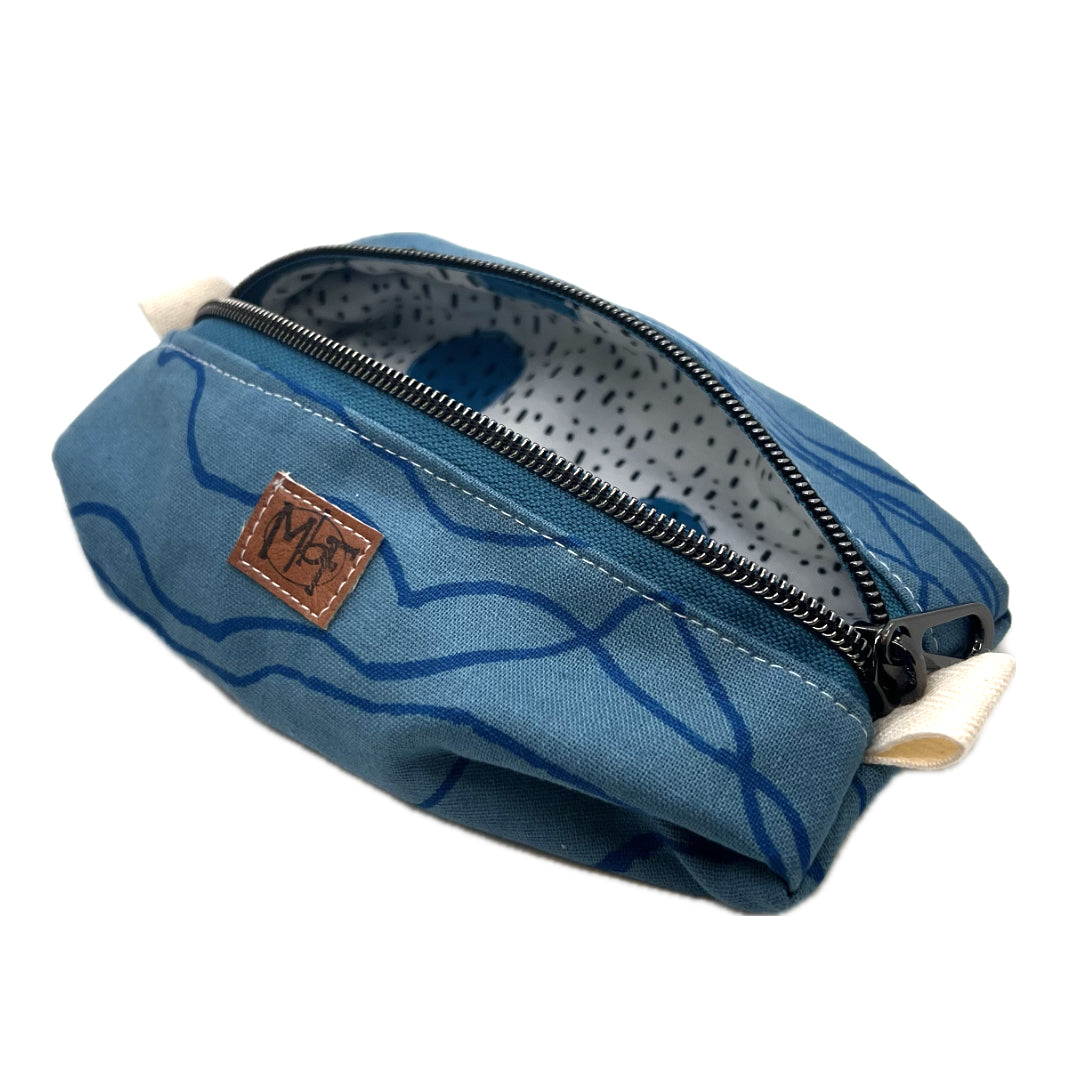 A zippered fabric pouch with dark blue wavy lines on a lighter blue background. The inside fabric has blue circles with black speckles on a white background. 